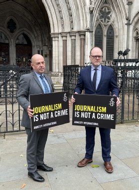Photo of journalists Barry McCaffrey (left) and Trevor Birney outside the High Court in London, holding signs that read: